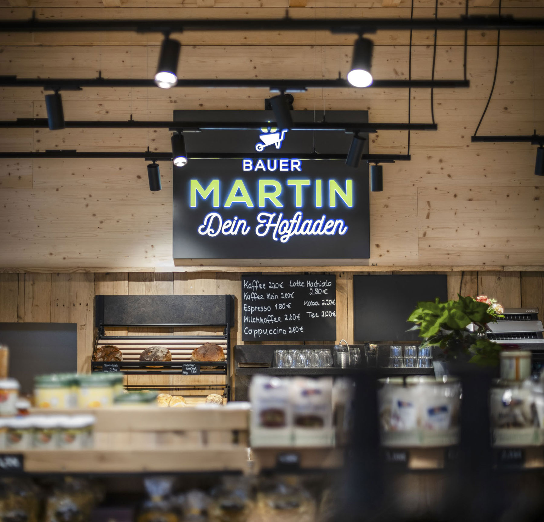 Blick in den Markt in Bambergen: Holzwand mit beleuchtetem Bauer-Martin-Schild, Brotregal und Kreidetafel
