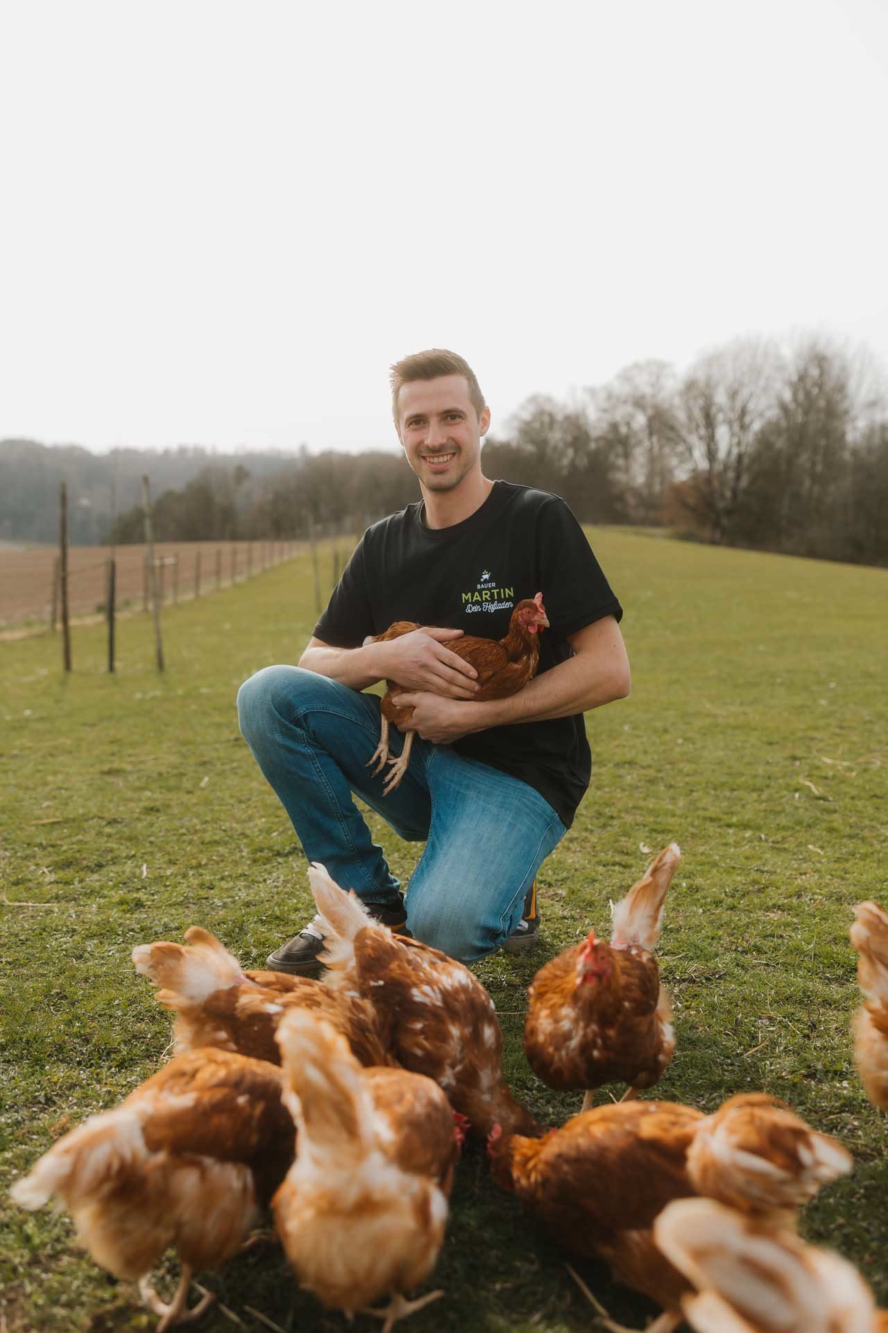 Simon Martin kniet auf der Wiese zwischen seinen Legehennen